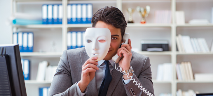 man half covering face with mask and smiling menacingly on the telephone depicting fraud